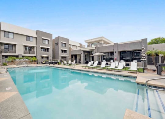 a swimming pool with chaise lounge chairs and umbrellas in front of a building