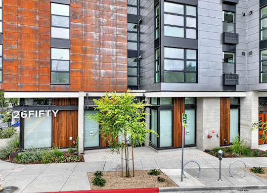 A modern building with a red brick facade and a tree in front at 26FIFTY Apartments, California