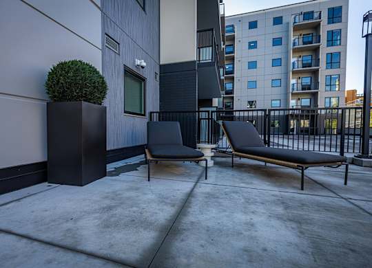 an apartment patio with two chairs and a plant on a black fence