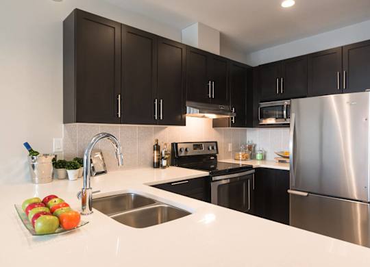 A kitchen with a stainless steel refrigerator and black cabinets.