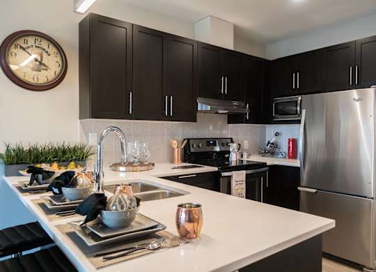 A modern kitchen with a stainless steel refrigerator and black cabinets.