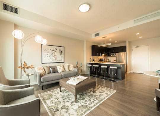A modern living room with a grey sofa, a grey armchair, a coffee table, and a bar area in the background.