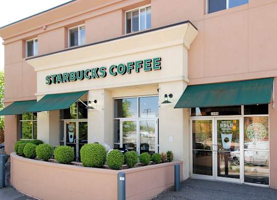 A Starbucks Coffee store with green awnings and a pink building.