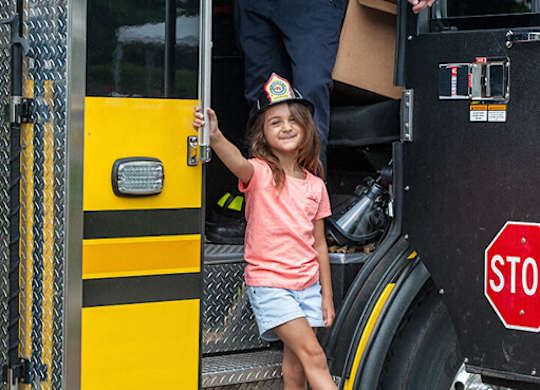 A little girl is standing on the step of a fire truck.