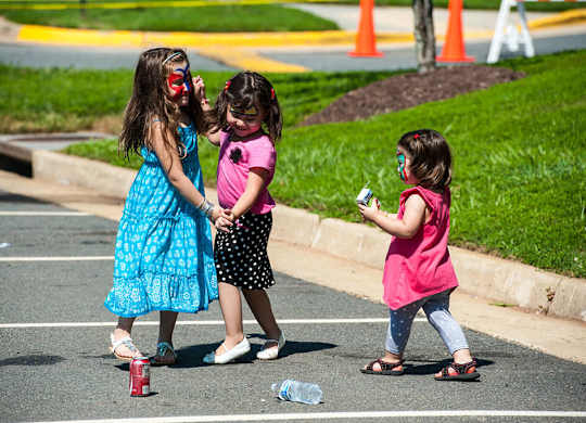 Three little girls playing with a bottle in a parking lot.