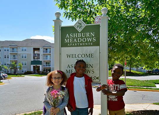 Three children stand in front of a sign that says Ashburn Meadows.
