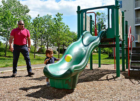 A child playing on a green slide with an adult standing nearby.