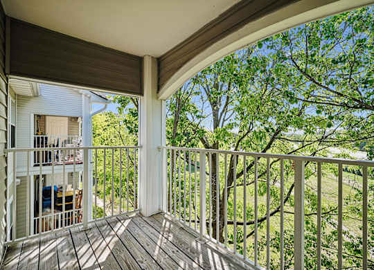 A balcony with a white railing and a view of trees.