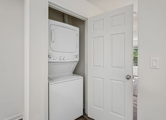 A white washing machine is in a small alcove in a white room.