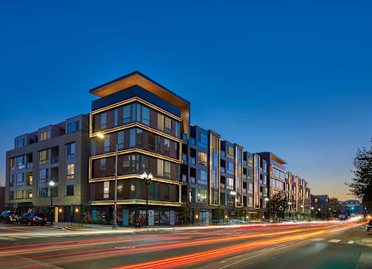 A long exposure shot of a modern apartment building at dusk with light trails from moving vehicles.