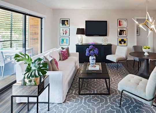 A living room with a white couch, a black coffee table, and a TV mounted on the wall.