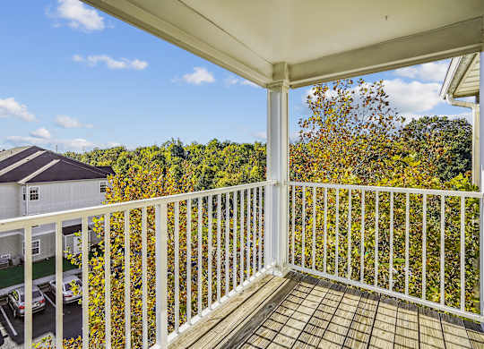 A balcony with a white railing overlooks a parking lot and a building.
