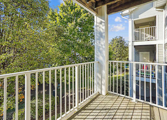A balcony with a white railing and a view of a tree and a house.