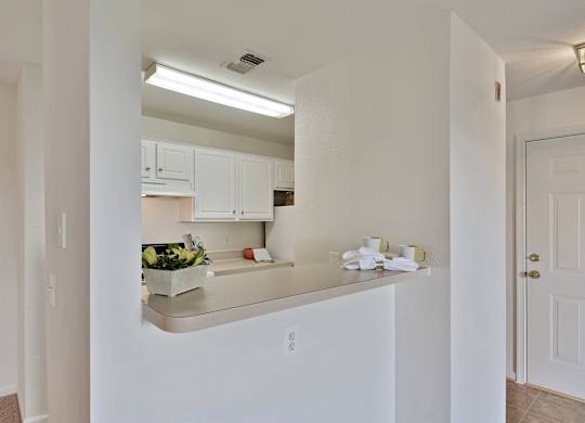 A kitchen with white cabinets and a countertop with a bowl of fruit on it.