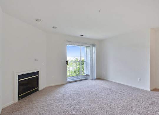 A large, empty room with a fireplace and sliding glass doors leading to a balcony.