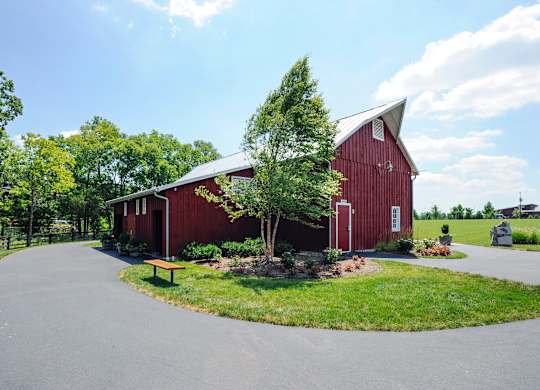 A red barn with a white door and windows is surrounded by a green lawn and trees.