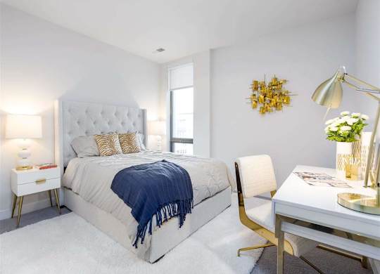 A bedroom with a large bed, a desk with a lamp, and a chair.
