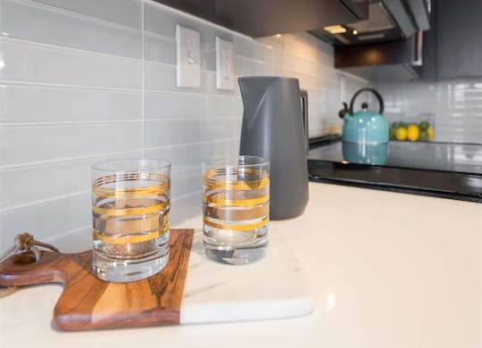 Two glasses of water are on a wooden tray in a kitchen.