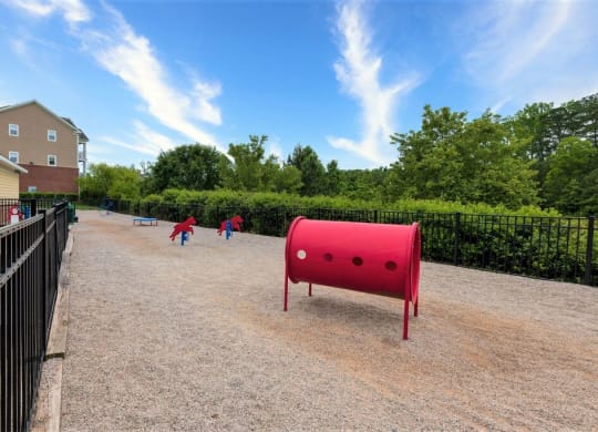 a large red barrel sits in the middle of a gravel path on a sunny day