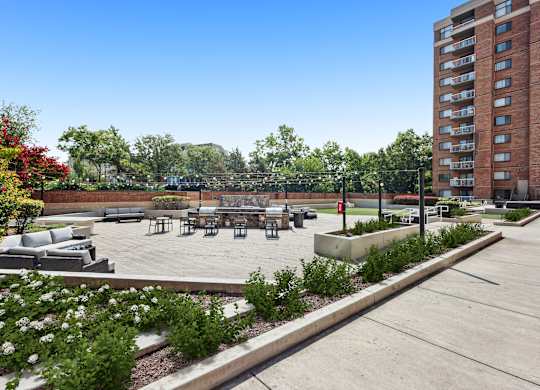 A large outdoor seating area with a concrete floor and a grassy area with a bench and a tree.