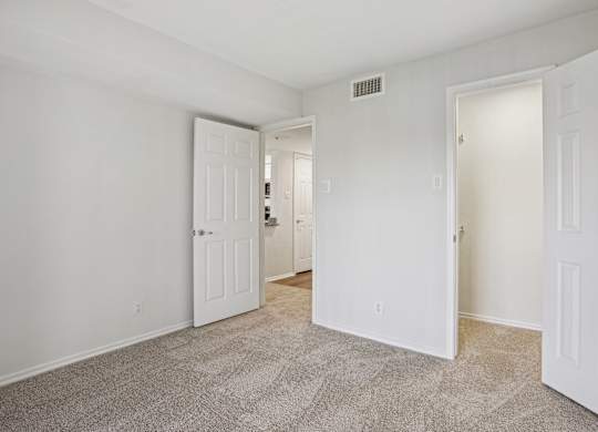 A room with carpeted floor and three white doors.