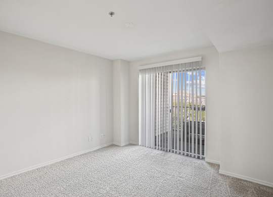 A white room with a carpeted floor and a window with blinds.
