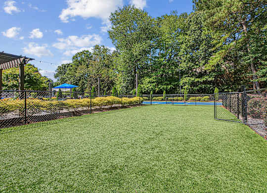 A green lawn with a tennis court surrounded by a fence.