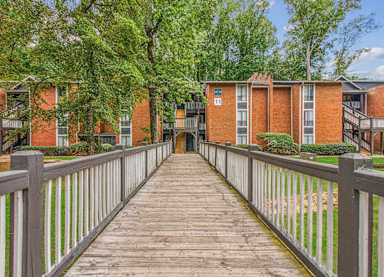 A wooden walkway leads to a brick building with a white fence on either side.