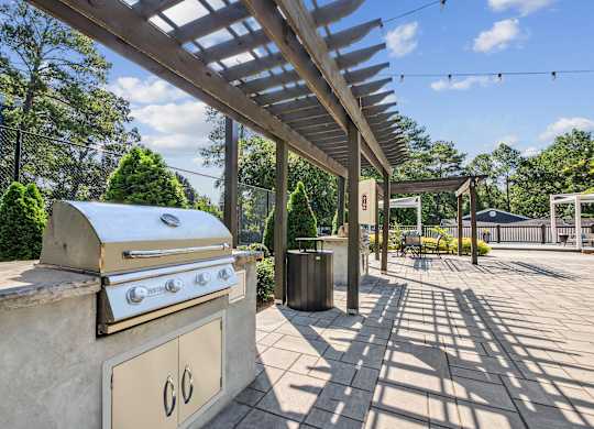 A BBQ grill is on a patio with a canopy over it.