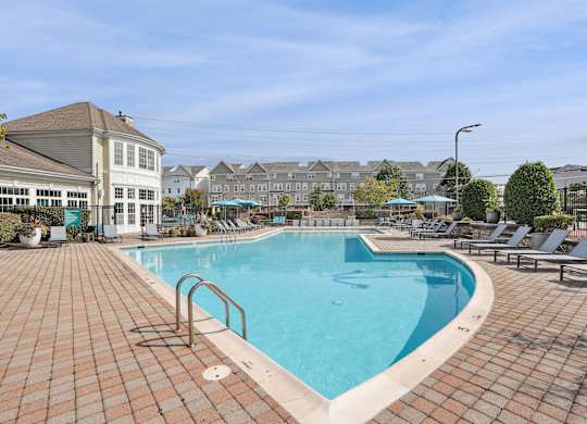A large outdoor swimming pool surrounded by a brick patio and lounge chairs at Elme Dulles, Herndon, VA