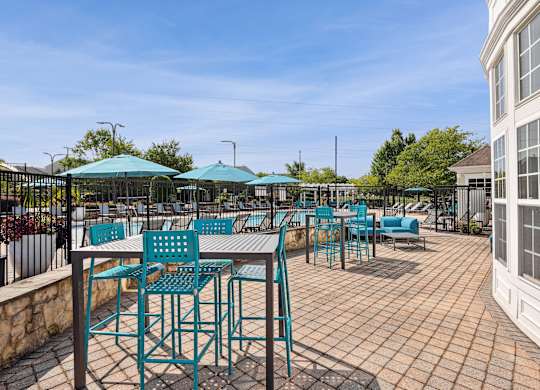 A patio with blue chairs and tables is surrounded by a white building and trees at Elme Dulles, Herndon, VA