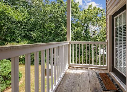 A wooden deck with a white railing and a brown doormat.