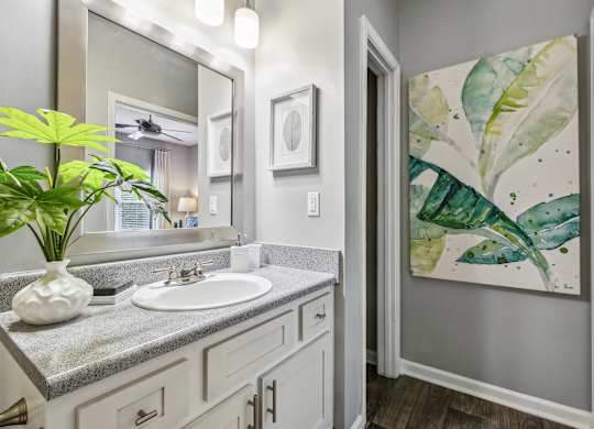 A bathroom with a sink, mirror, and a painting of a leafy plant.