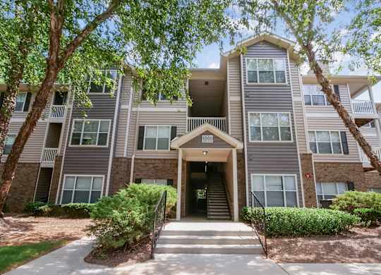 A large apartment building with a front entrance and a tree in front.