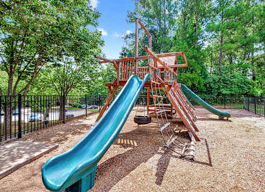 A playground with a green slide and a red wooden structure.