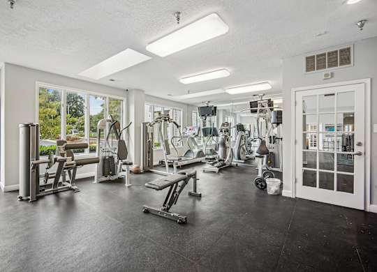 A spacious gym with a variety of equipment and a view of the outdoors through the windows.
