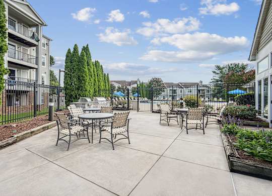 A patio with a table and chairs is surrounded by a fence and has a pool in the background.