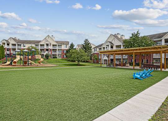A playground with a slide and a green lawn in front of apartment buildings.