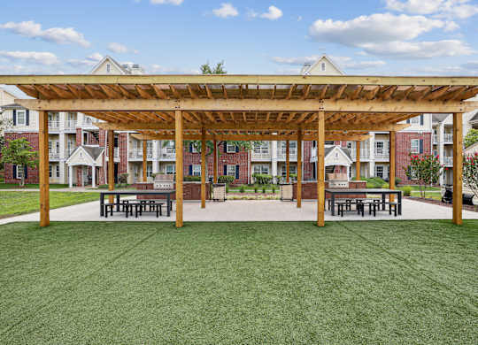 A wooden pergola is over a picnic table in a grassy area.