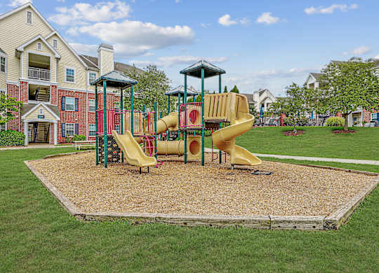 A playground with a yellow slide in the middle of a grassy area.