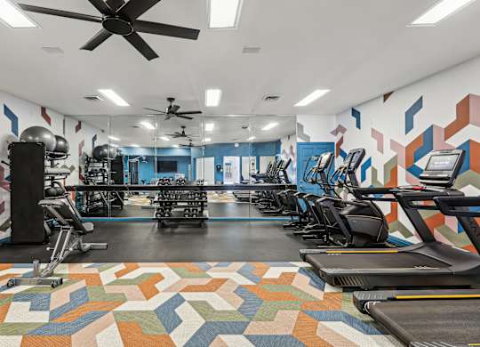 A gym with a variety of equipment including treadmills, elliptical machines, and a fan.