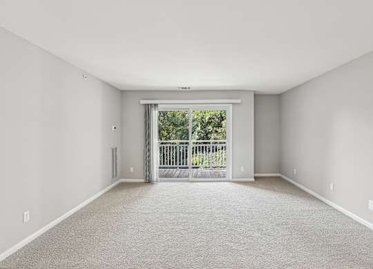 A spacious room with a carpeted floor and a sliding glass door leading to a balcony.