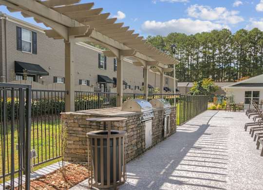 A sunny day at the outdoor seating area of a building with a row of chairs and a trash can.