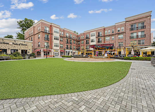 A large grassy area in front of a building with a brick walkway at Elme Watkins Mill, Gaithersburg