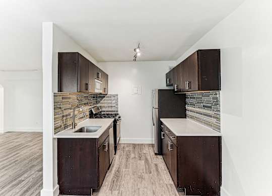 A kitchen with dark wood cabinets and a stone backsplash.