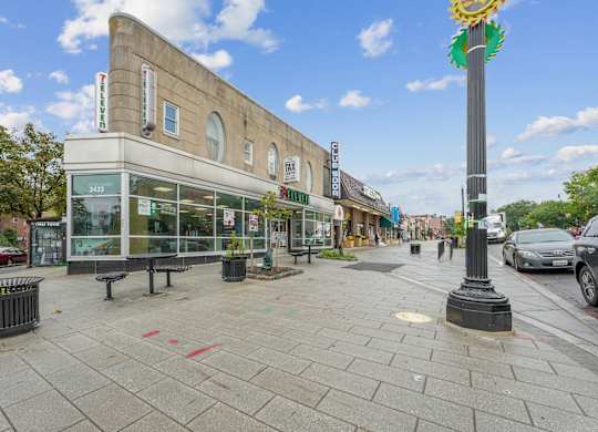 A street view with a building on the left and a pole with a flower on top on the right.