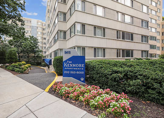 The entrance to The Kenmore Apartments with a blue sign and flowers in the foreground.