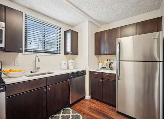 A kitchen with a refrigerator on the right and a sink with a bowl of fruit on the counter at Riverside Apartments, Alexandria, Virginia