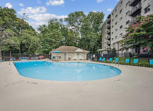 A small pool with a blue tinted water surrounded by trees and a building in the background  at Roosevelt Towers, Falls Church, VA