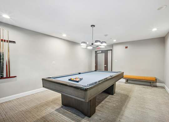 A pool table is in the middle of a room with a bench and a door  at Roosevelt Towers, Falls Church, VA